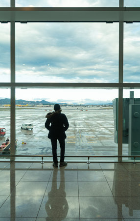 woman standing at a large airport window looking out onto the runway. Waiting for her flight.の写真素材