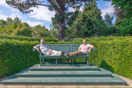 Bodnant Garden, Conwy, Wales, United Kingdom - July 19, 2018: Two men sitting on a giant oversized bench, Bodnant garden, Conwy, Walesのeditorial素材