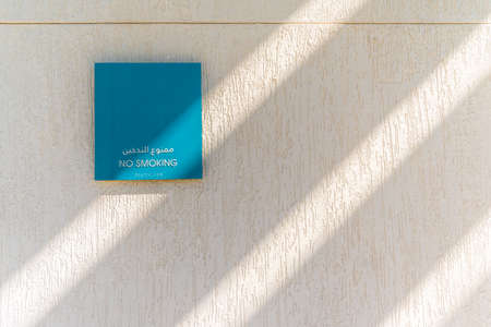 A blue no smoking sign on textured white wall and rays of sunlight, Umm Al Emarat Park, Abu Dhabi, United Arab Emiratesの写真素材