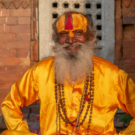 Tilanga, Kathmandu, Nepal - April 2, 2019: one sadhu al dressed in silky saffron yellow clothing, smiling at the camera, taken at the end of the afternoon of a spring sunny day at the Pashupatinath templeのeditorial素材