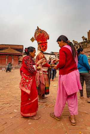Bhaktapur, Nepal - April 5, 2019: Man wearing traditional mask and clothes and two women giving him offerings, taken in an overcast morning in the historical center of Bhaktapurのeditorial素材