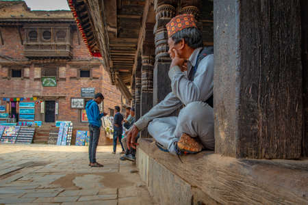 Bhaktapur, Nepal - April 5, 2019: Old man with traditional nepalese hat staring at passersby taken during an overcast afternoon in the historical center of Bhaktapurのeditorial素材