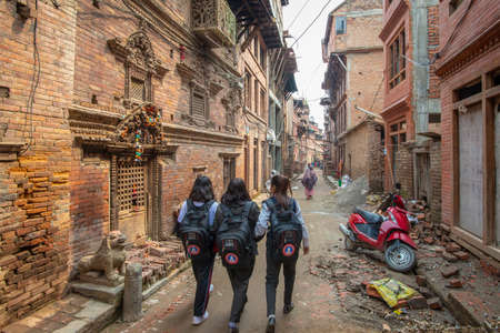 Bhaktapur, Nepal - April 5, 2019: Three school girl walking down a narrow street taken during an overcast afternoon in the historical center of Bhaktapurのeditorial素材