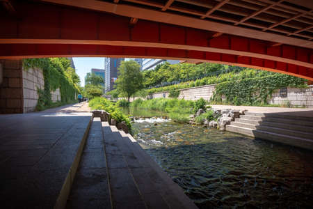 Seoul, South Korea - May 31, 2019: A man is walking along the Cheonggyecheon stream, viewed from underneath a vermilion red bridgeのeditorial素材