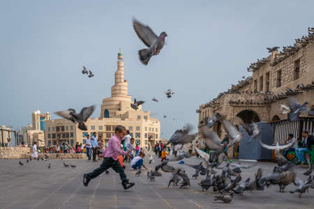 Doha, Qatar - 25 Nov 2016: Young boy running after a large number of pigeons. Taken on late fall day afternoon in Souq Wakif, Dohaのeditorial素材