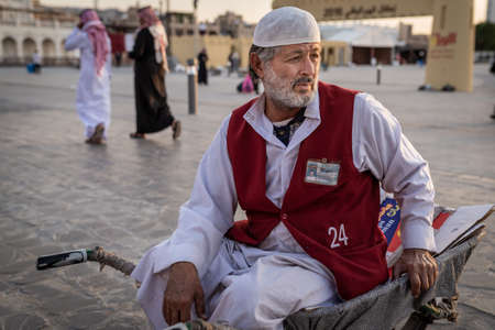 Doha, Qatar - 17 Dec 2016: A man porter is waiting for his next customer while seating on a...