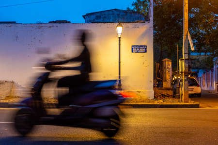Pondicherry, India - March 19, 2018: Unrecognisable man riding a scooter is passing by a street sign...