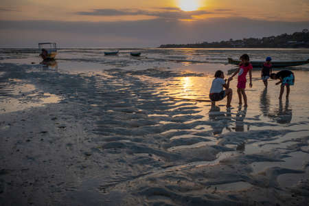 Nusa Ceningan, Bali, Indonesia - May 18, 2018: Boats stranded on sand at sunset, with four kidsのeditorial素材