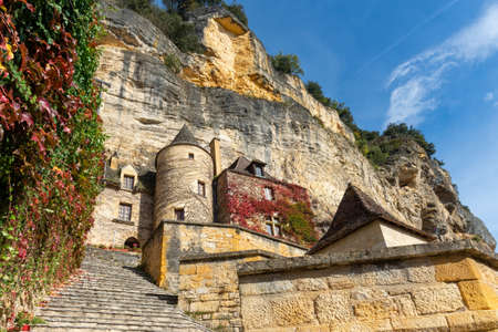 Limestone cliff and historic houses made of yellow stones of La Roque-Gageac, Perigord, taken on a sunny autumn afternoonの写真素材