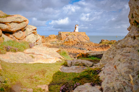 A small lighthouse off the Main island and red cliffs in the foreground. Taken on a partly sunny summer day, Brehat Island, Brittany, France.の写真素材