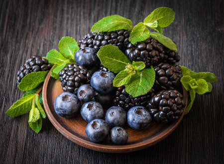 blackberries, blueberries, mint on a wooden plate, on a dark backgroundの写真素材