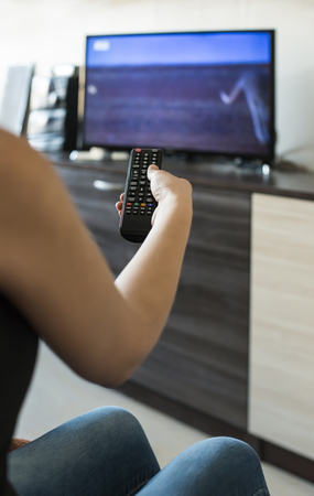 Woman hold TV remote control. TV on the background.