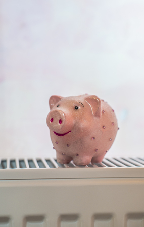Piggy money box on heater at home. Energy consumption savings concept. Pink pig on radiator.の写真素材