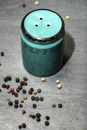 Black pepper shaker and beans on stone dark table. Multi colour pepper beans around green papper...