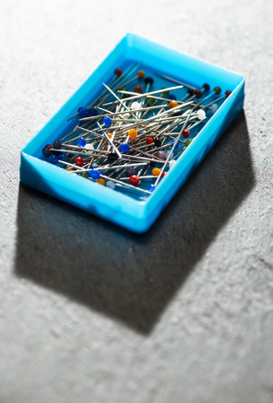 Small box with sewing pins. Many multi colored needles. Authentic light. Blades and pricking concept. Fashion industry metaphor.の写真素材