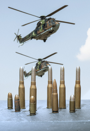 Military helicopter in the blue cloudy sky. Cartridges and ammunition in the foreground.