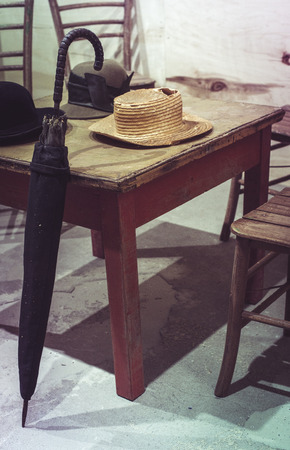Old umbrella and hats on a vintage table. Red Vintage style wooden table and chairs. Pastel tones.の写真素材