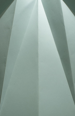 Folded green colour paper. Pastel tones. Hard natural light. Folds and wrinkles on paper. Geometric shapes and figures on the paper.の写真素材