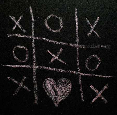 Tic-tac-toe game on black board. Valentines day concept with tic tac toy symbols written with chalk....
