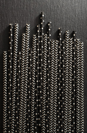 Black contrast drinking straws. Background of patterned straws on dark stone table. Arranged straws next to each other. Concept for Summer time and drinking. Geometric backdrop.の写真素材