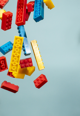 Floating Plastic geometric cubes in the air. Construction toys on geometric shapes falling down in motion.  Blue pastel background. Children's toys. Circle geometric shapes on plastic bricks.の写真素材