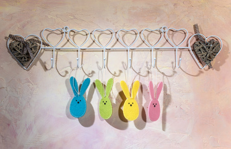 Easter bunny hooked on the wall in a room. Multi Colored easter rabbits made of fabric on pink wall. Hard light from window and shadows on the wall. White vintage hanger.の写真素材
