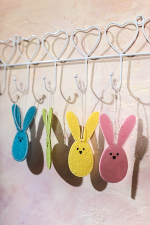Easter bunny hooked on the wall in a room. Multi Colored easter rabbits made of fabric on pink wall. Hard light from window and shadows on the wall. White vintage hanger.の写真素材