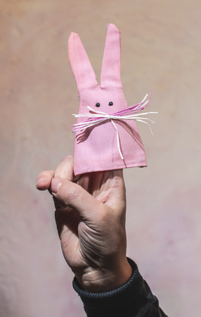Pink Easter bunny made of cloth hooked on hand. Pink wall background. Easter concept with abstract rabbit.の写真素材