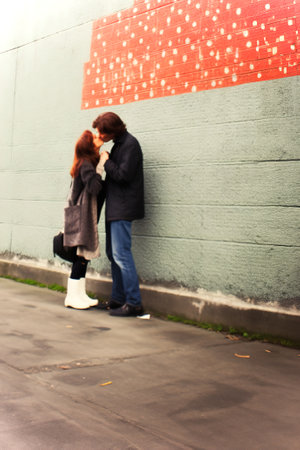 Young man and a woman are kissing, leaning against a wall.の素材