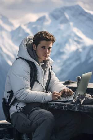 A man programmer coding on a laptop computer high in the mountain snowy hill. Remote work on mountain top. Sunny day.の素材