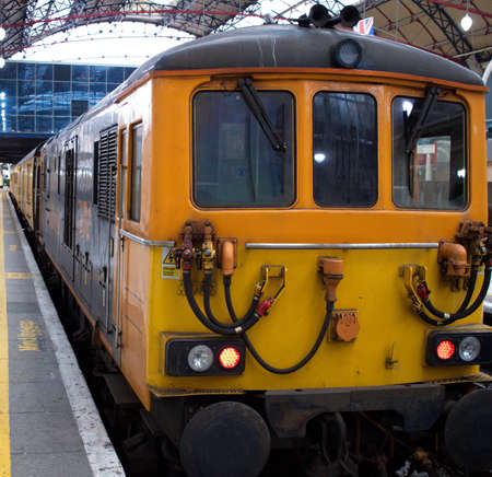 Orange modern cargo train parked at train station in London, with some dirt and soot, and the English flag partly in the background.のeditorial素材