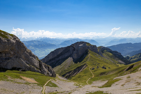 Amazing view of mountain ranges with dirt foot path leading into them at the thinnest pointの写真素材