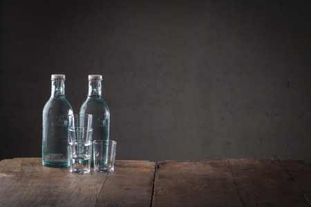 Two bottles of beverage on a rustic counter top with a stack of clean glasses or tumblers and copy space to the side on a dark backgroundの写真素材