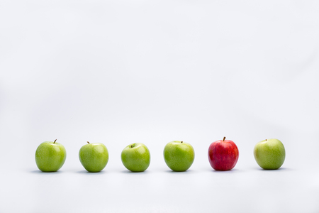 One ripe red apple in a line of fresh green apples in a concept of diversity, individualism and leadership, on a white background with copy spaceの写真素材