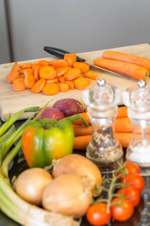 Preparing a healthy meal with fresh vegetables arranged ready on a kitchen table with a salt and pepper mill with focus to a large knife and freshly diced carrots in the backgroundの写真素材