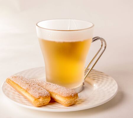 Close up on pair of delicious sponge biscuits and hot yellow tea on plate over bright tableの写真素材