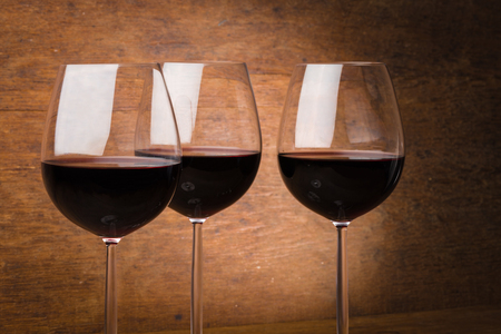 Three fine wine glasses half full with liquid over brown wooden background with spotlight effectの写真素材