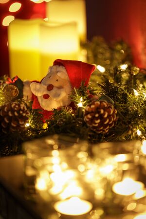 Burning candles with Christmas wreath and a cute little Santa in a seasonal holiday still life to decorate the homeの写真素材