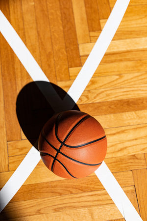 Basketball on a wooden parquet court floor with white lines and hard shadow.