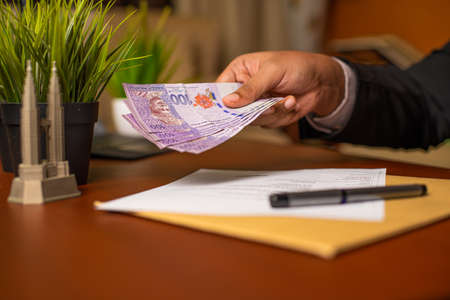 Corrupt Businessman or CEO or Politician hands giving bribe money after signing documents or contracts on an office desk. Venality, bribe, corruption concept.の写真素材