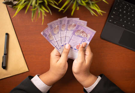 Businessman or CEO or Politician hands holding bribe money on an office desk. Venality, bribe, corruption concept.の写真素材