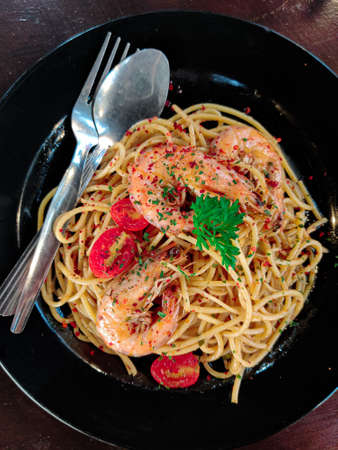 Delicious seafood Aglio Olio with big prawns on a black plate. Top viewの写真素材