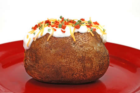 Baked potato loaded with butter, sour cream, cheddar cheese, bacon bits, and chives.  Isolated on white background.の写真素材