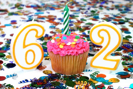 Number 62 celebration cupcake with candle and sprinkles.  Confetti in background.の写真素材