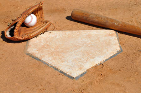 Baseball, glove, and bat on home plate. 