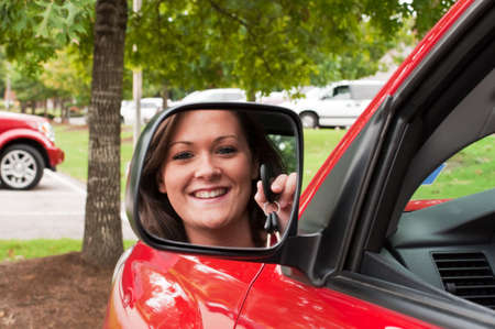 Attractive young brunette holding vehicle keys in rear view mirror.の写真素材