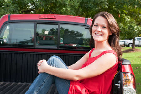 Attractive female brunette sitting in bed of red pickup truck. の写真素材