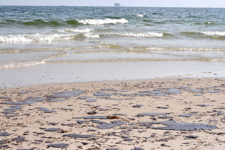 Oil spill on beach with off shore oil rig in background.の写真素材