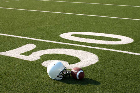 American football and helmet on field next to 50 yard line.の写真素材
