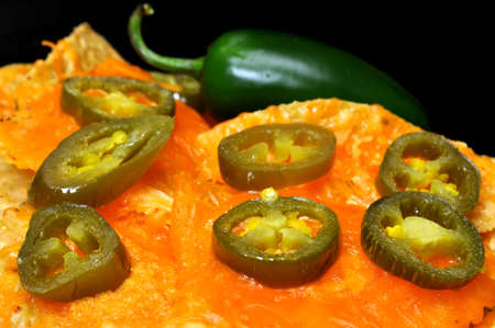 Closeup of nachos with jalapeno pepper slices.  Isolated on black background.の写真素材
